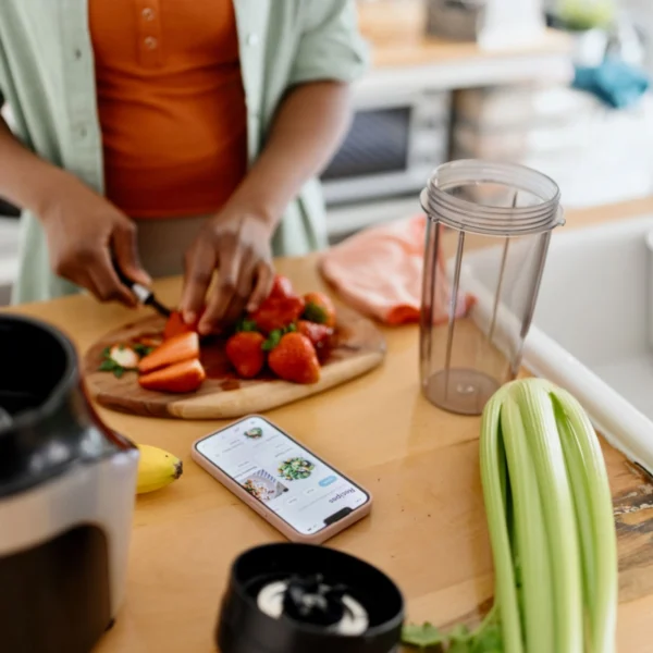 Person preparing fruits beside phone and blender.