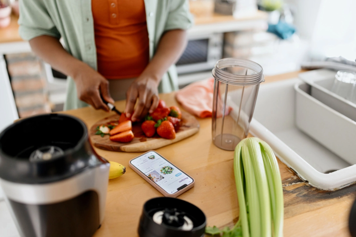 Person preparing fruits beside phone and blender.