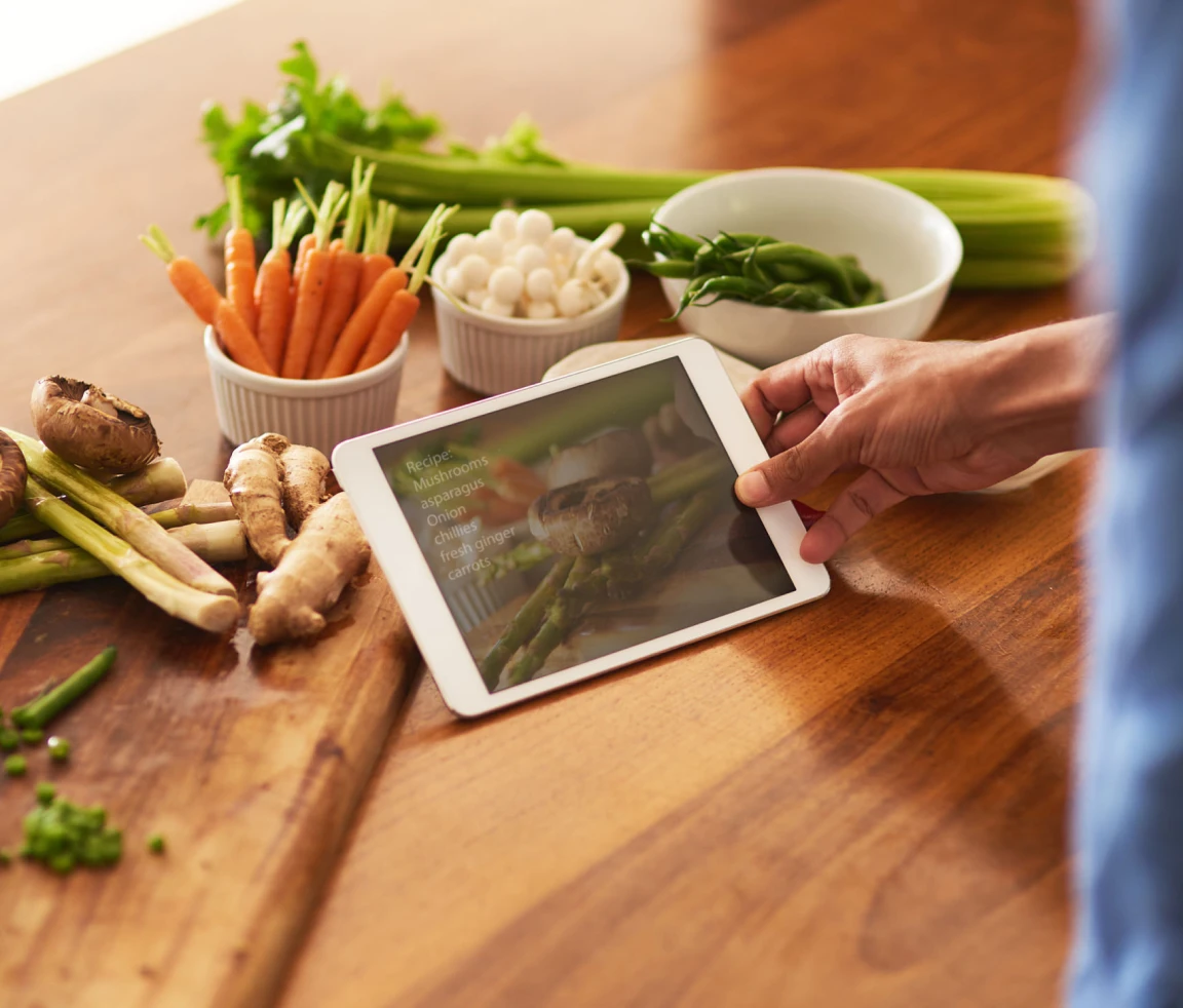Tablet with vegetables on wooden kitchen counter.