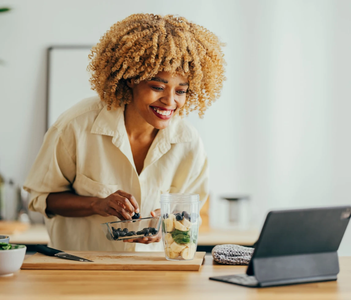 Woman preparing smoothie while watching a tablet.