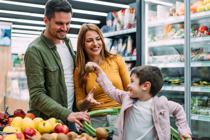 Shot of a cute little boy and his mom and dad shopping in a grocery store. Happy parents grocery shopping with their small son at the supermarket.
